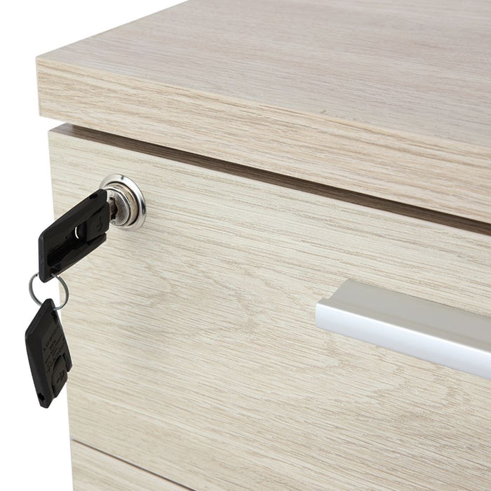 Desk height pedestal front with keyed cam lock and metal pull on light wood surface