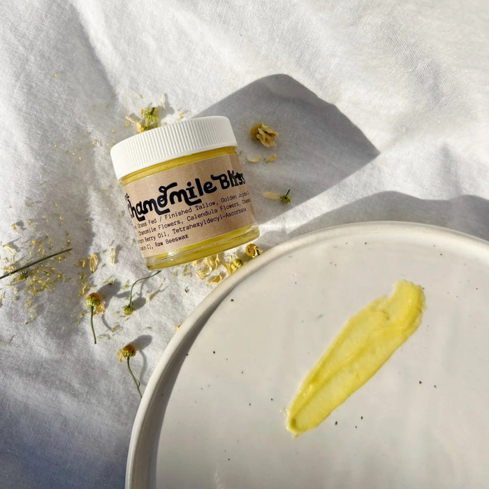 Jar of cream with a yellow chamomile tallow on a white surface