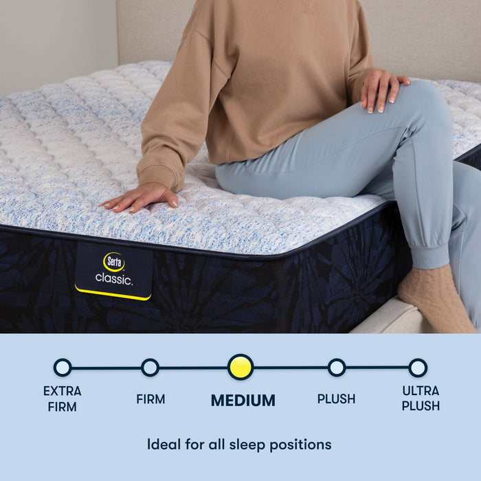 Woman sitting on a Serta classic medium mattress with her right hand placed on the mattress ||feel: medium ||level: standard